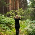 Waldbaden Person im dichten Farnwald, Hände am Hinterkopf, in einer achtsamen Haltung.