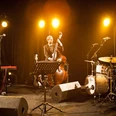 grammophon-jazzband-25810.jpg Jazzband mit Kontrabass, Schlagzeug und Klavier auf einer Bühne im warmen Scheinwerferlicht.
