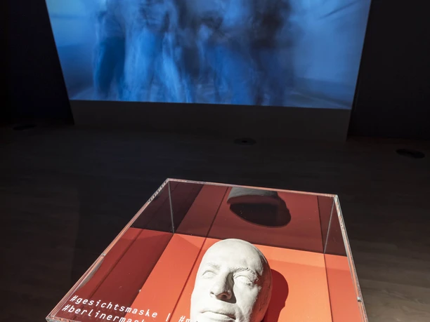 Dance Museum of the German Dance Archive Cologne Plastic face mask in a display case in front of a blue projection image in the exhibition room.