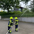 Feuerwehr Kinder Strassweg Zwei Kinder in Hückeswagener Kinderfeuerwehr-Uniformen sprühen Wasser mit einem Feuerwehrschlauch.