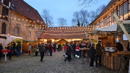 Besucher auf dem Adventsmarkt im beleuchteten Innenhof der historischen Wasserburg Gebhardshagen.