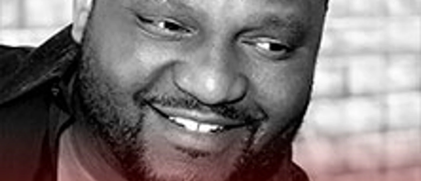 Porträt eines lächelnden Mannes vor unscharfem Hintergrund mit Schriftzug Aries Spears Euro Trip
