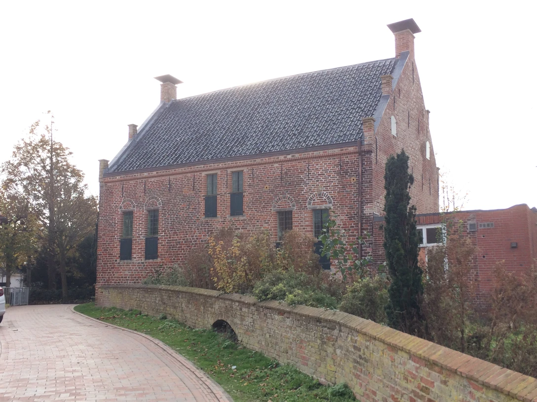 Steinhaus Greetsiel Backsteinbau mit hohem Satteldach, kleinen Fenstern und grünen Läden an einer gepflasterten Gasse.