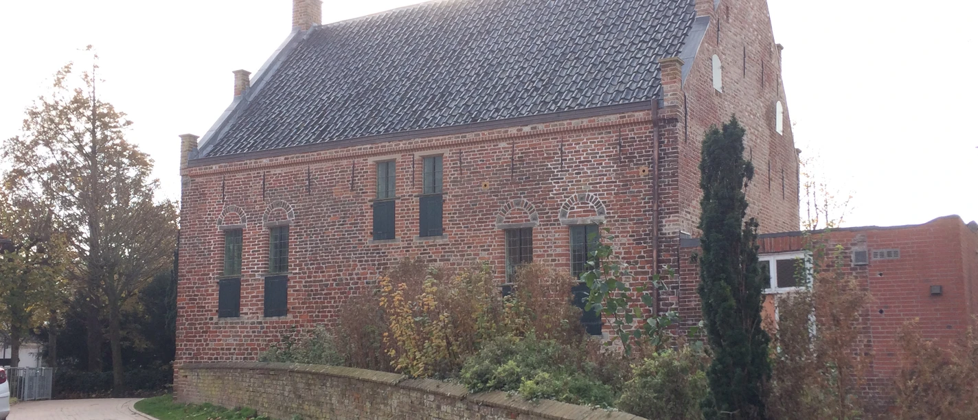 Steinhaus Greetsiel Backsteinbau mit hohem Satteldach, kleinen Fenstern und grünen Läden an einer gepflasterten Gasse.