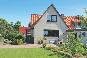 Ferienwohnung Bartel Außenansicht Helles Klinkerhaus mit rotem Dach, davor eine blaue Bank auf der gepflasterten Terrasse.