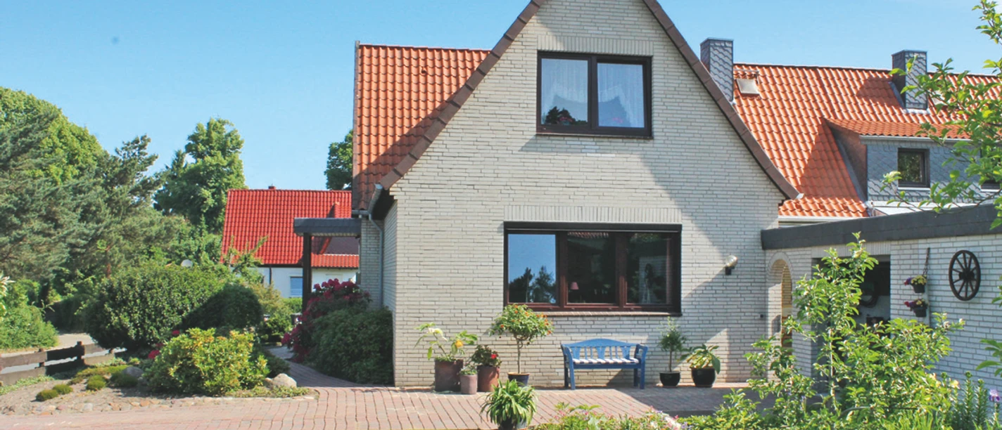 Ferienwohnung Bartel Außenansicht Helles Klinkerhaus mit rotem Dach, davor eine blaue Bank auf der gepflasterten Terrasse.