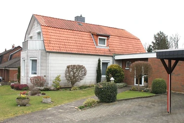 Ferienwohnung Gutt Außenansicht Hellgraues Haus mit rotem Dach, Balkon, grünem Vorgarten und gepflasterter Einfahrt.