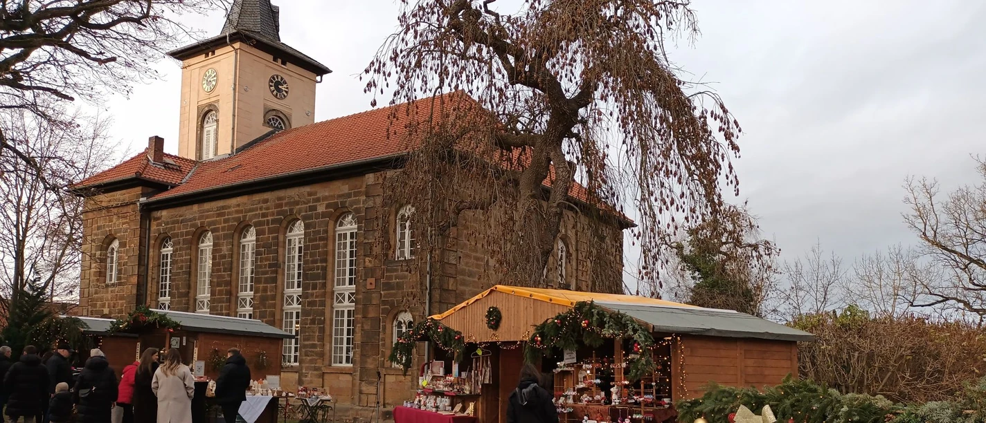 2025_Weihnachtsmarkt_Gitter_HD_16zu9.jpg Weihnachtsmarktbuden vor historischer Kirche in Salzgitter-Gitter mit Besuchern.
