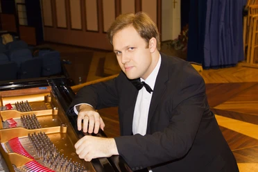 Alexey Chernov Pianist Alexey Chernov im schwarzen Anzug mit Fliege lehnt entspannt am Flügel.