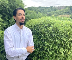Rubén Russo Pianist Rubén Russo im weißen Hemd vor einer grünen Hecke und Waldlandschaft.