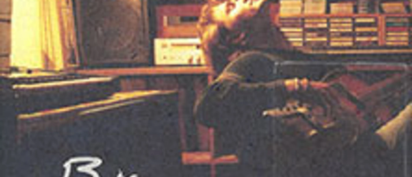 Verschachteltes Studio mit Musiker auf Stuhl und Gitarre in warmem Licht.