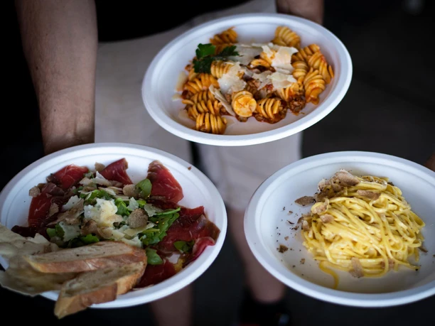 Drei weiße Teller mit Pasta und Carpaccio werden nebeneinander in Händen getragen.