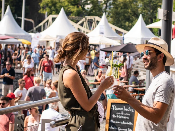 Gourmet Festival at the Chocolate Museum in Cologne Two people toast with drinks, surrounded by festival stands and the public.