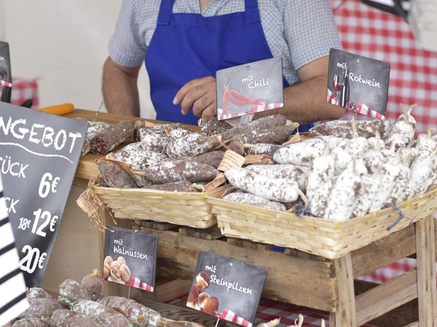 Gourmet Festival am Schokoladenmuseum in Köln Mann mit Schürze verkauft verschiedene Wurstsorten an einem Marktstand mit Preisschildern.