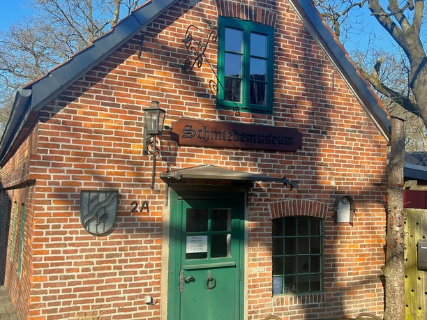 Backsteinhaus des Beckedorfer Schmiedemuseums mit grüner Tür und Schild am Eingang.