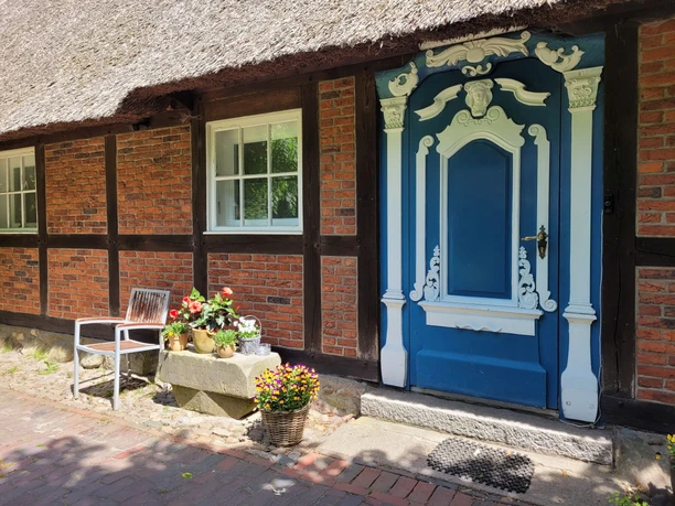 Marschenhaus Gesundheitspark Speckenbüttel 20230531_132006 (c) Tanja Mehl_Erlebnis Bremerhaven_WEB.jpg Historisches Reetdachhaus mit aufwendig verzierter blauer Eingangstür und Ziegelfassade.