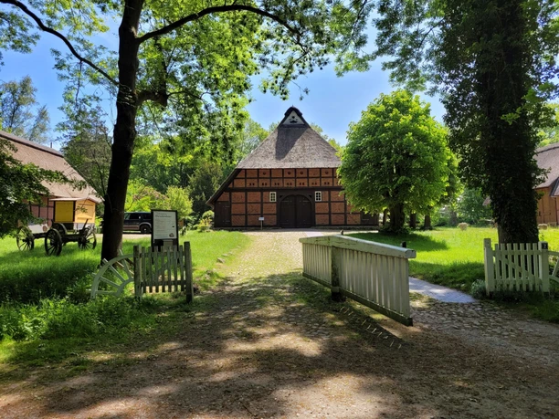 Marschenhaus Gesundheitspark Speckenbüttel 20230531_131530 (c) Tanja Mehl_Erlebnis Bremerhaven_WEB.jpg Historisches Fachwerkhaus mit Reetdach, großer Einfahrtstür und umgeben von Bäumen.