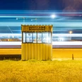 Exhibition "Störungen, starke Störungen" Small yellow protective cabin in front of nocturnal industry with bright horizontal light trails.