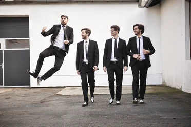 Kaiserbeats Pressefoto 2017.jpg Vier Musiker in schwarzen Anzügen, einer springt vor heller Hauswand.