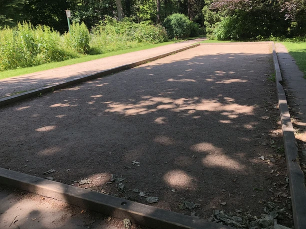 Boule Speckenbütteler Park (c) Mailin Knoke (3)_WEB.jpg Gepflegte Boulebahn mit Sandbelag im Grünen, umrahmt von Bäumen und Büschen im Park.