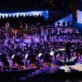 Ensembles: Philharmonie Südwestfalen & Band Großes Orchester auf beleuchteter Bühne mit Dirigent und Chor im Hintergrund