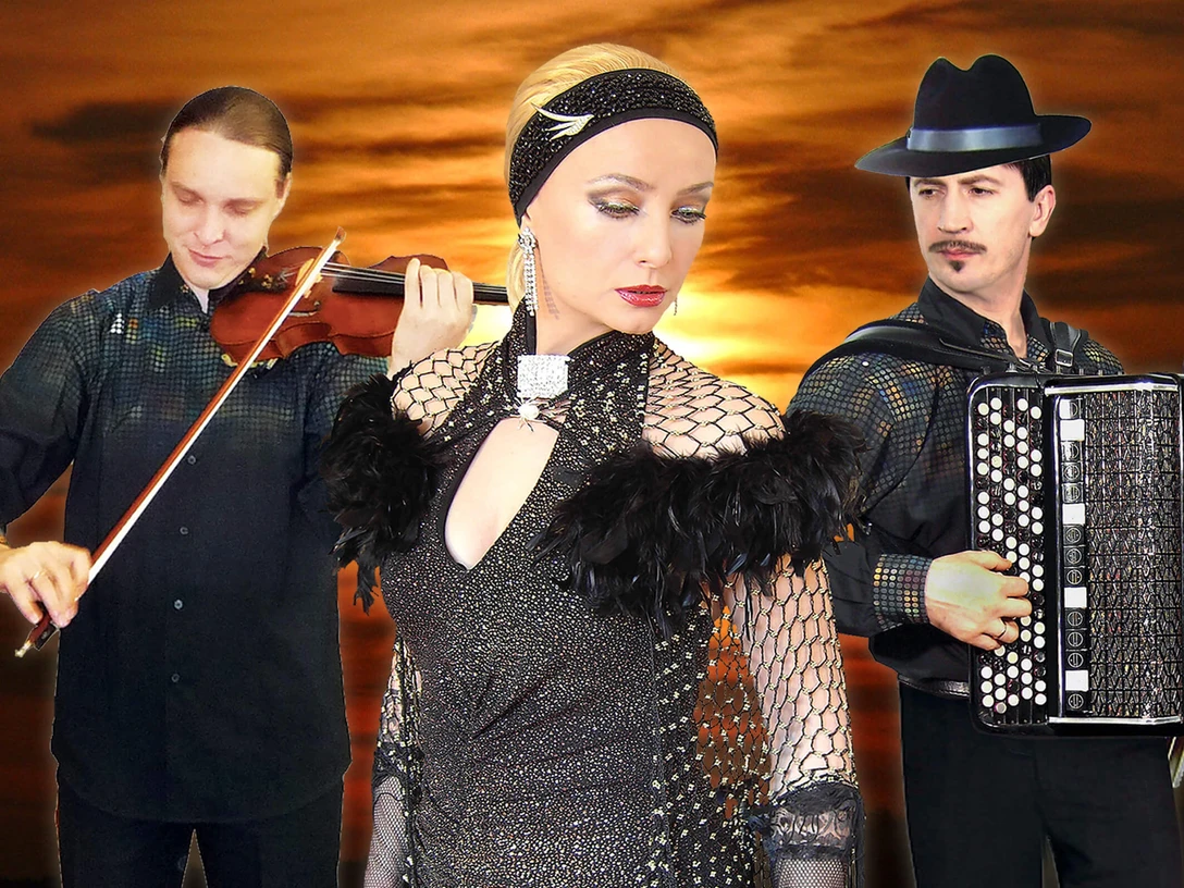 grandoni-trio.jpg Das Foto zeigt das Grandoni-Trio bei einem Sonnenuntergang. Links ein Geiger, rechts ein Akkordeonist und in der Mitte eine Sängerin in einem glitzernden Kleid. Die Farben im Hintergrund sind warm und dramatisch, was der Komposition eine elegante und sinnliche Atmosphäre verleiht.