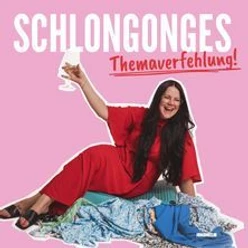 Frau in rotem Outfit lacht, hält ein Glas und sitzt auf Kleidung vor rosa Hintergrund.