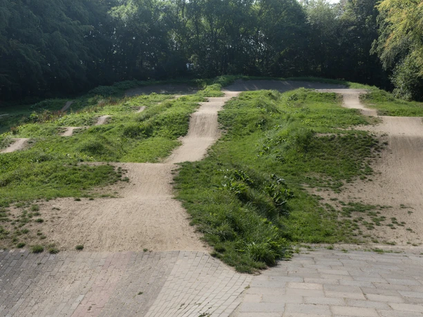 BMX-Bahn P7343 (c) Helmut Gross_Erlebnis Bremerhaven_WEB.jpg Hügelige BMX-Sandpiste im Grünen mit mehreren Fahrspuren und Sprüngen, umgeben von Bäumen.