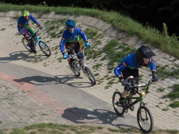 BMX-Bahn P7371 (c) Helmut Gross_Erlebnis Bremerhaven_WEB.jpg Drei BMX-Fahrer in voller Montur fahren rasant durch eine gepflasterte Steilkurve.