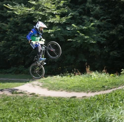 BMX-Bahn P7393 (c) Helmut Gross_Erlebnis Bremerhaven_WEB.jpg Junge Person springt mit BMX-Fahrrad auf einer Dirt-Strecke vor grünem Hintergrund.