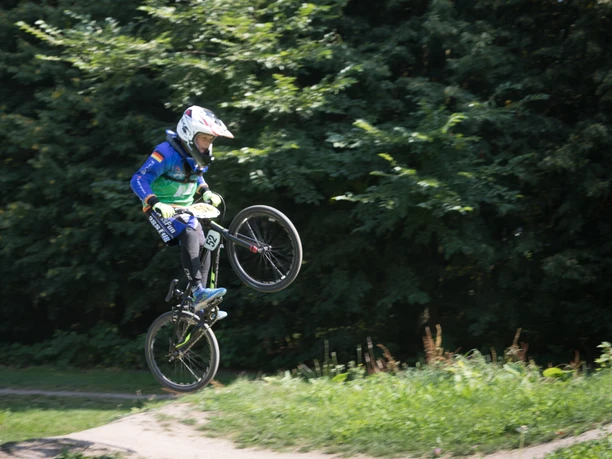 BMX-Bahn P7393 (c) Helmut Gross_Erlebnis Bremerhaven_WEB.jpg Junge Person springt mit BMX-Fahrrad auf einer Dirt-Strecke vor grünem Hintergrund.