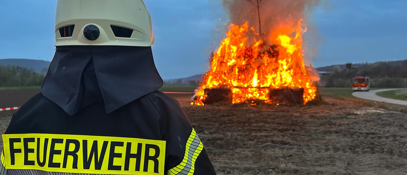 Osterfeuer.JPEG Feuerwehrkraft überwacht loderndes Osterfeuer in der Dämerung auf freiem Feld.