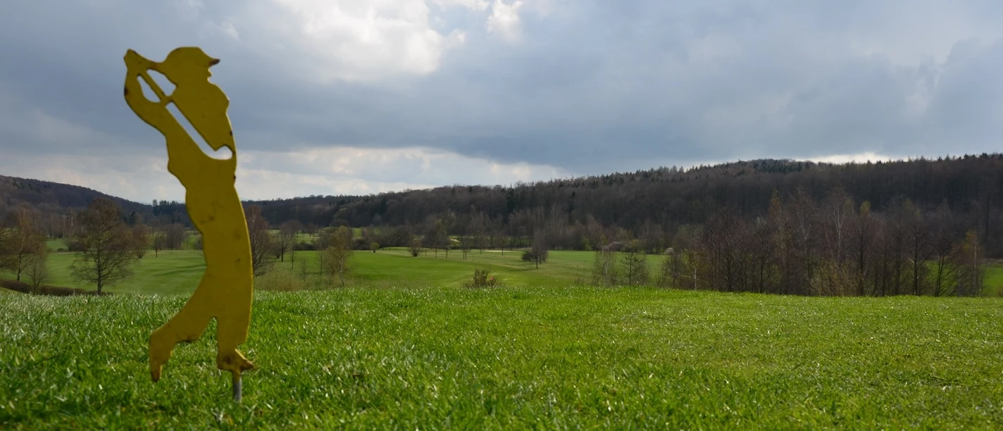 Golfplatz_Salzgitter (31)_HD_16zu9.JPG Gelbe Silhouette eines Golfers im Vordergrund vor grüner Golfplatzlandschaft unter bewölktem Himmel.