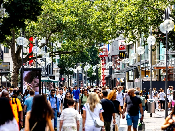 Schildergasse Belebte Einkaufsstraße mit vielen Passanten, Geschäften und Schatten großer Bäume
