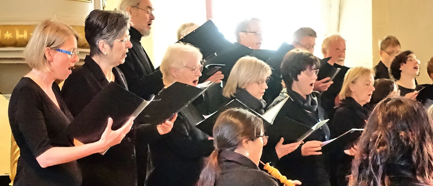 DSC04769_HDR deep shodow.jpg Ein gemischter Chor in schwarzer Kleidung singt konzentriert in einer Kirche, begleitet von Musikern.