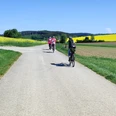 Radeln und Kultur Radfahrende auf einem Weg durch weitläufige Felder unter blauem Himmel.