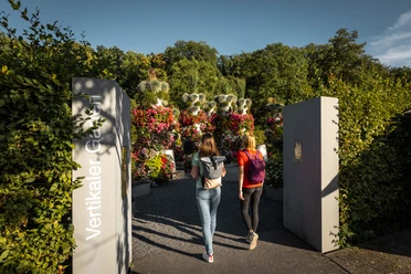 O-Schatz-Park-Freizeitpark-Region-Leipzig-Garten-Eingang-Ausflug-Philipp-Herfort-Photography-leipzig-travel.jpg Eingang zum O-Schatz-Park, zwei Frauen gehen hinein, im Hintergrund blühen bunte Blumen und verschiedene Pflanzen.