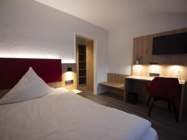 Zimmer in der Waldklause Modernes Hotelzimmer mit Doppelbett, Schreibtisch, TV und Holzdetails