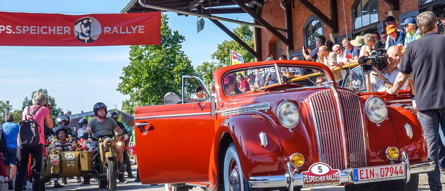 Einbecker_Oldtimertage_STIFTUNG_PS.SPEICHER_Marcus_Yannikakis (5).jpg Ein roter Oldtimer-Cabrio bei der PS.SPEICHER Rallye, umgeben von Zuschauern am Straßenrand.