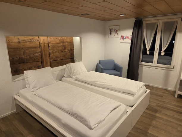Modernes Doppelzimmer im Gasthof Krone Luthern mit zwei Betten, Holzelementen, Sessel und geschmackvoller Wanddekoration, freundliche und helle Einrichtung.