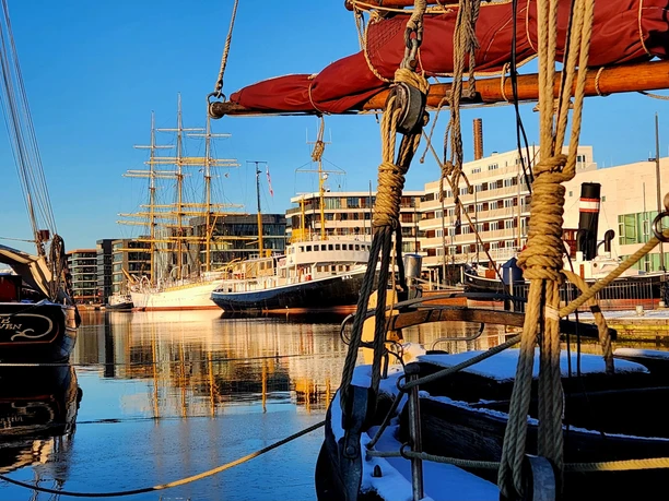 20240109_151039 (c) Dagmar Brandenburg_Erlebnis Bremerhaven_WEB.jpg Blick über Traditionsschiffhecks auf den Neuen Hafen mit dem Dampf-Eisbrecher Wal und dem Windjammer Schulschiff Deutschland
