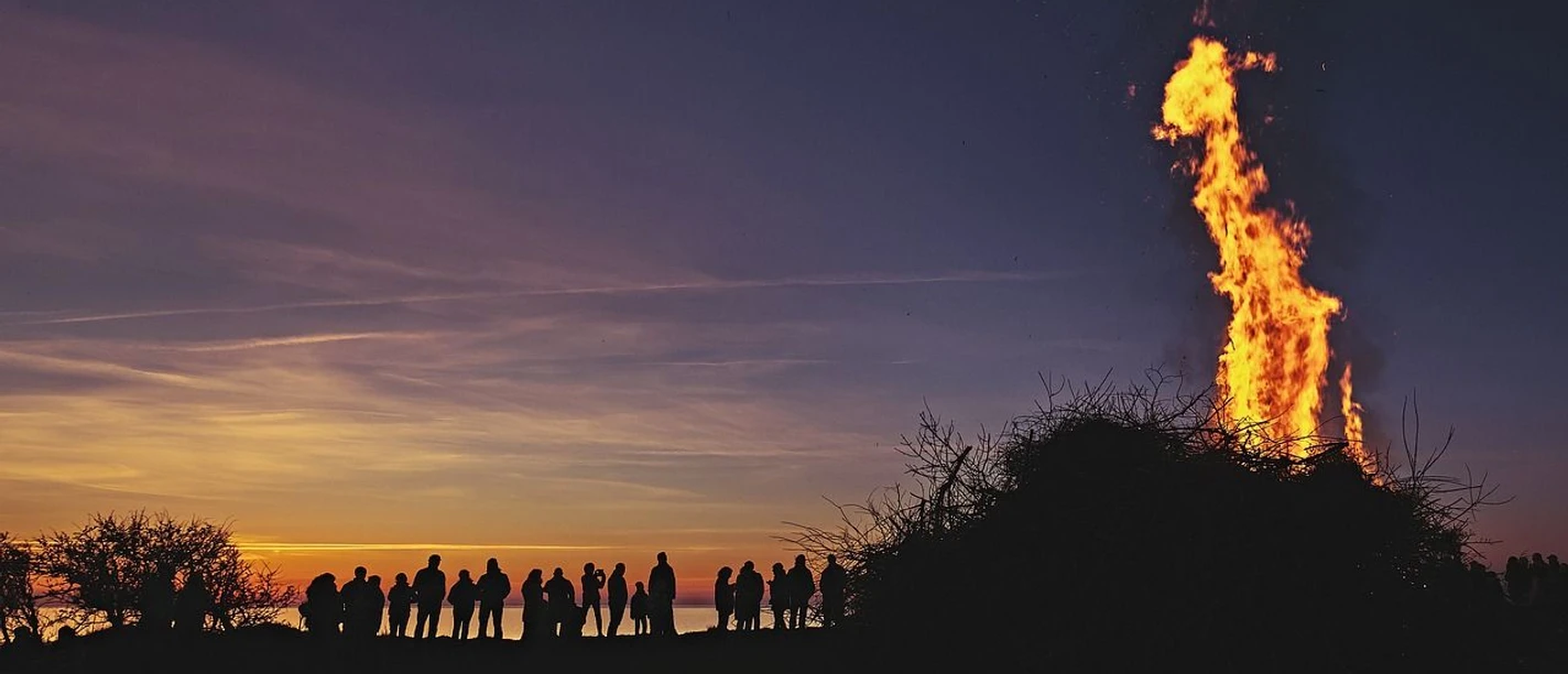 Osterfeuer Hohes Osterfeuer in der Dämmerung, umringt von Zuschauern vor einem farbintensiven Abendhimmel.