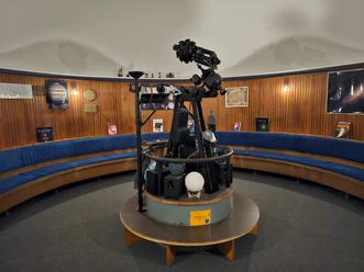 Inneres des Planetariums Bremerhaven mit Projektor, blauen Sitzbänken und astronomischen Postern.