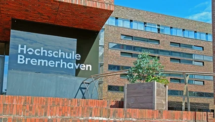 Campus_HochschuleBremerhaven (2)_WEB.jpg Schild mit der Aufschrift "Hochschule Bremerhaven" vor einem modernen Klinkergebäude bei Sonnenschein.