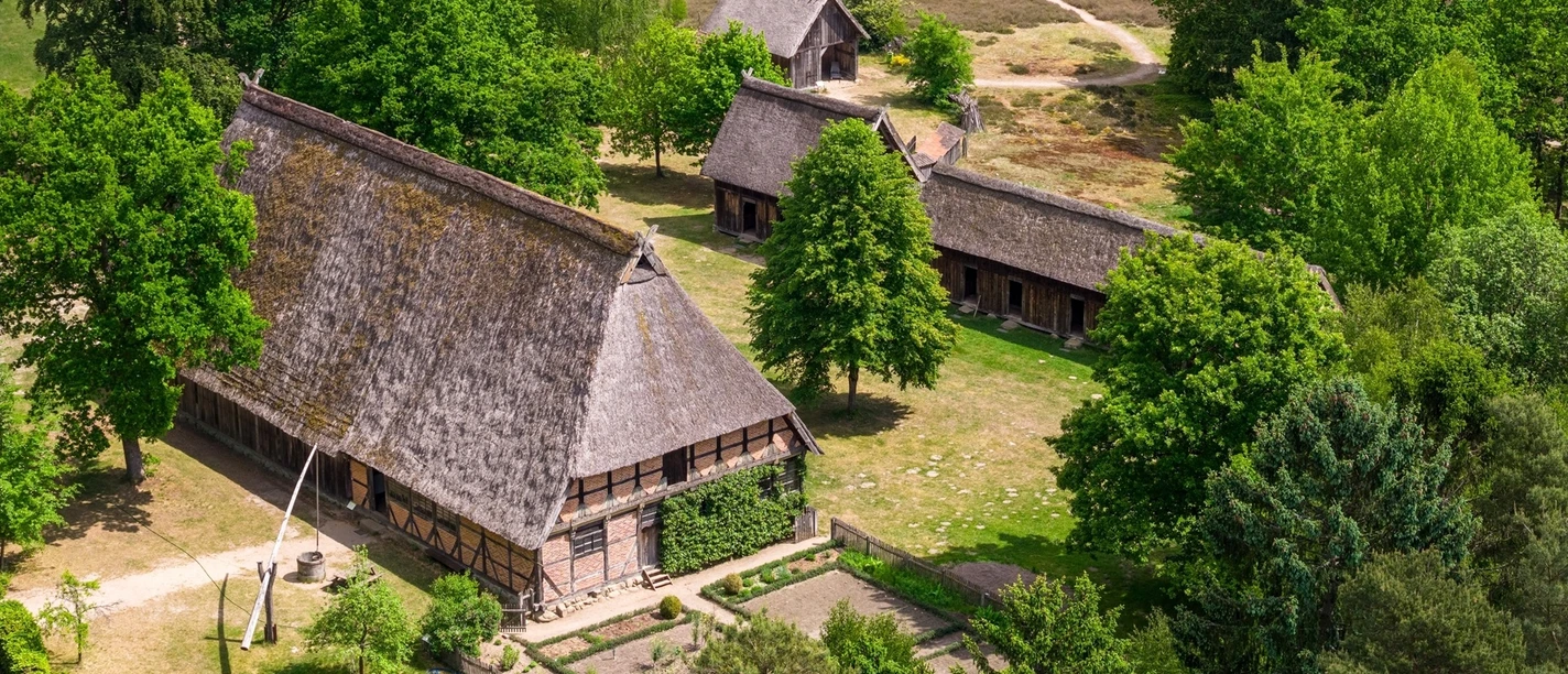 hauptbild-museumsdorf-hoesseringen-fotocredits-thorsten-scherz-1920x1080px.jpg Luftaufnahme historischer Reetdach-Fachwerkhäuser im grünen Museumsdorf Hösseringen.