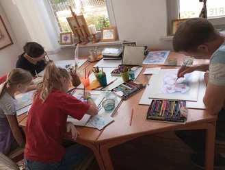 M_Ac.jpg Erwachsene und Kinder malen konzentriert mit Stiften und Farben an einem Tisch im Atelier.