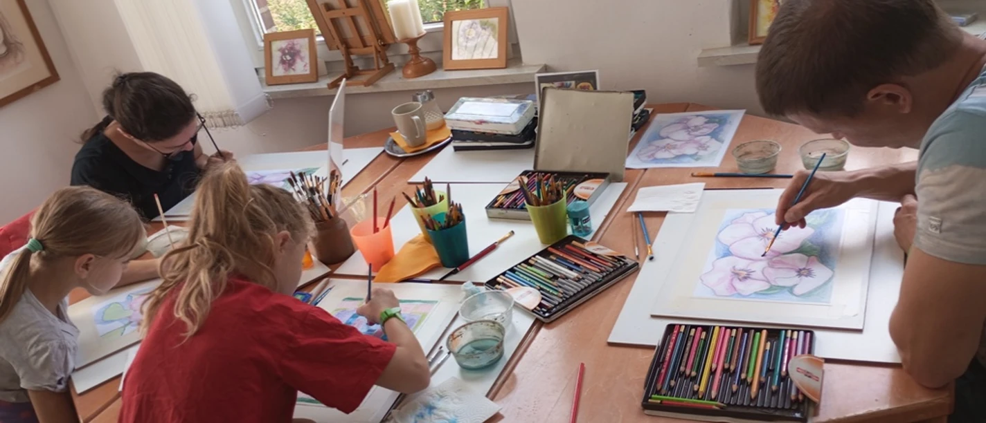 M_Ac.jpg Erwachsene und Kinder malen konzentriert mit Stiften und Farben an einem Tisch im Atelier.