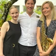 Summer Sounds.png Drei lachende Musiker, ein Mann und zwei Frauen, stehen draußen nebeneinander. Eine hält ein Saxophon.