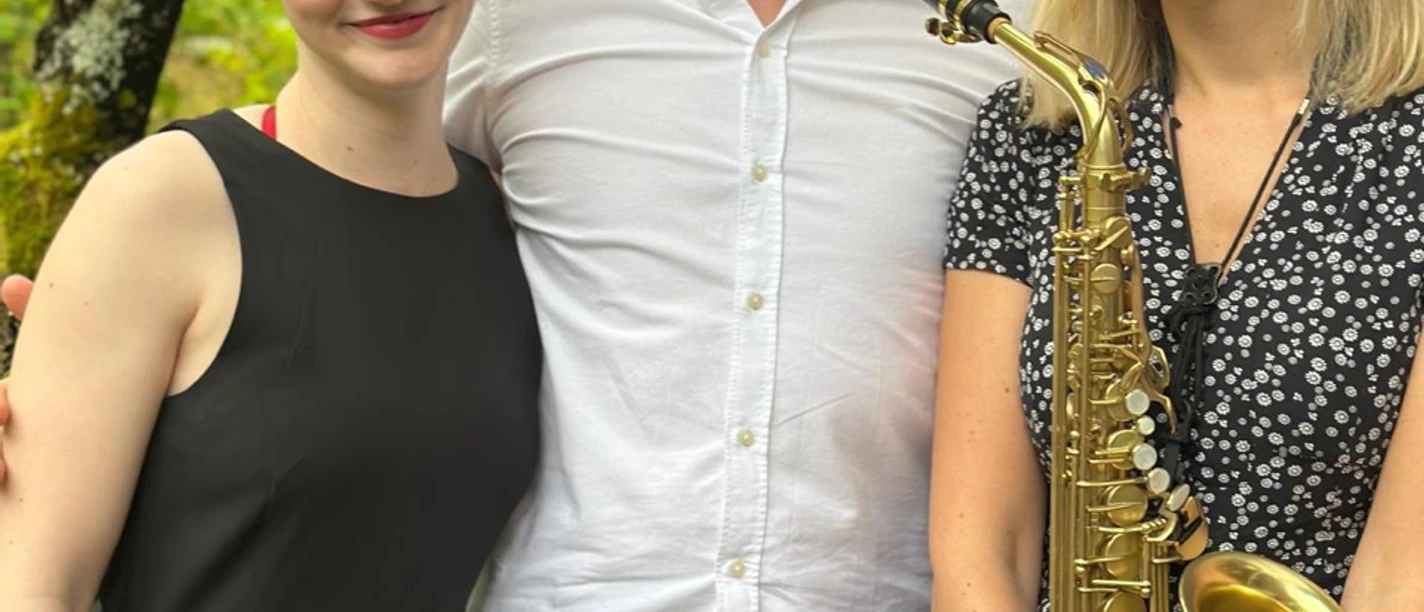 Summer Sounds.png Drei lachende Musiker, ein Mann und zwei Frauen, stehen draußen nebeneinander. Eine hält ein Saxophon.