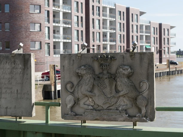 Gedenktafel Schleuse Neuer Hafen M6459 (c) Helmut Gross_Erlebnis Bremerhaven_WEB.jpg Zwei steinerne Gedenktafeln mit Inschrift und Löwenwappen vor einem Hafenbecken.